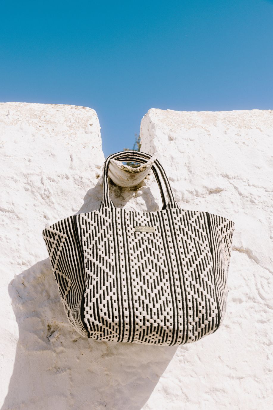 Black and cream patterned tote bag displayed on whitewashed steps beneath a clear blue sky.