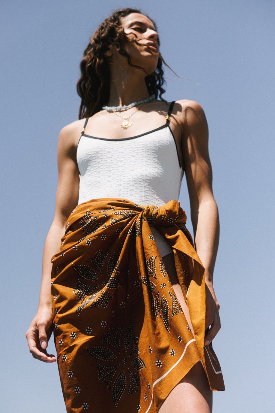 Woman wearing a brick printed pareo tied at the waist over a white swimsuit against a clear blue sky.